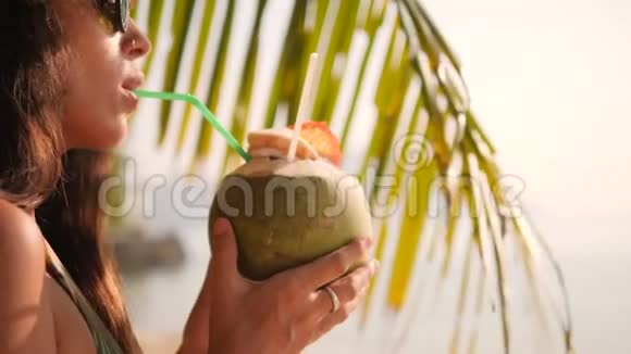 吸引人的混合种族年轻旅游少女在热带海滩喝新鲜泰国椰子水鸡尾酒4K视频的预览图