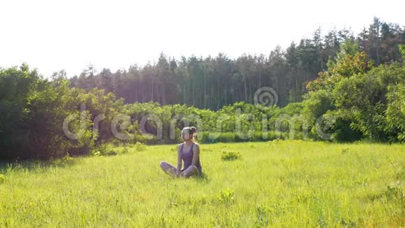 幸福的年轻女子坐在风景名胜区的绿色草坪上背景是夕阳视频的预览图
