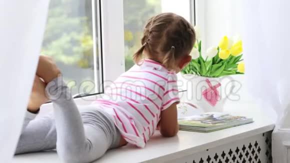 特写小可爱女孩在家窗台上看书的画像视频的预览图