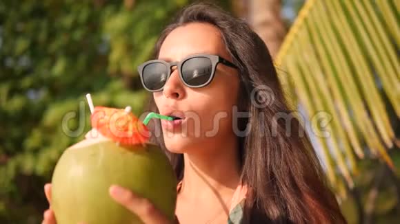 吸引人的混合种族年轻旅游少女在热带海滩喝新鲜泰国椰子水鸡尾酒4K视频的预览图