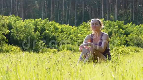 幸福的年轻女子坐在风景名胜区的绿色草坪上背景是夕阳视频的预览图