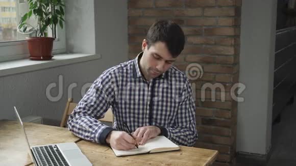 漂亮的男人穿着衬衫在日记里做笔记看着笔记本电脑视频的预览图