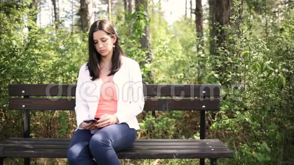 迷人的微笑的年轻女人带着智能手机在公园里滑动滑块视频的预览图