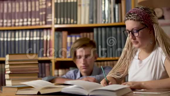 漂亮的女孩正在图书馆的一张桌子上写作视频的预览图