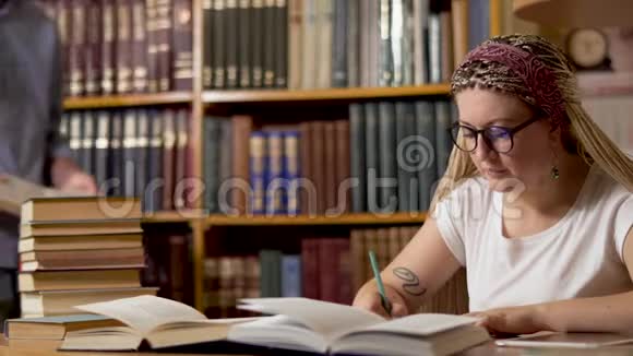 漂亮的女孩正在图书馆的一张桌子上写作视频的预览图