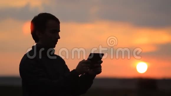 在游戏中玩平板电脑的人背景上美丽的日落视频的预览图