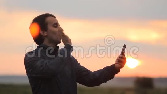 一个男人在电话里打视频电话背景上美丽的日落视频的预览图