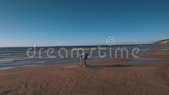 日落时在海滩上做瑜伽的人的空中视野视频的预览图