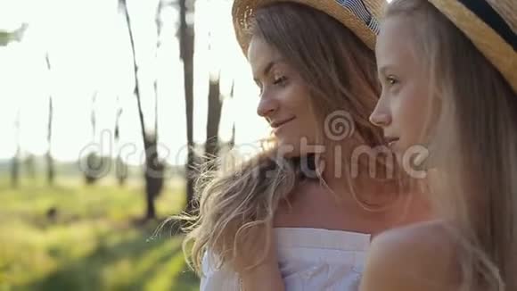日落时分穿着白色连衣裙和草帽在树林里玩耍的母亲和女儿快乐视频的预览图