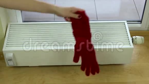 女孩手把红色羊毛手套放在家里的散热器上视频的预览图