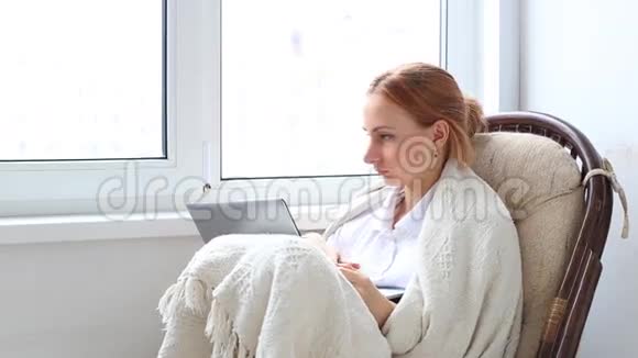 女人在客厅里的白色柳条椅上放松在手提电脑上工作视频的预览图