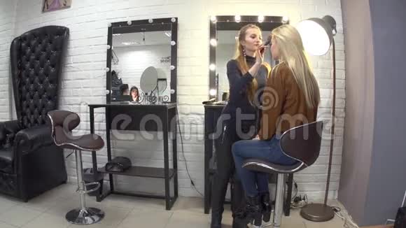 年轻的造型师给漂亮的金发女孩化妆视频的预览图