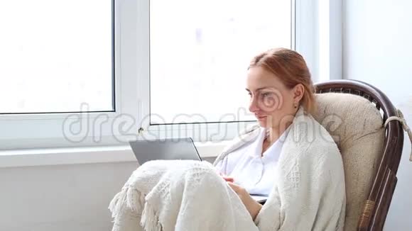 女人在客厅里的白色柳条椅上放松在手提电脑上工作视频的预览图