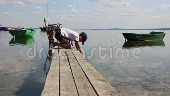 男孩在船附近的码头上洗脚视频的预览图