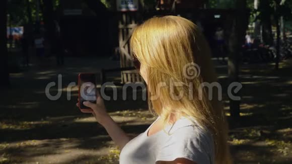 夏天在阳光下女人带着手机去公园4k慢镜头标准镜头视频的预览图