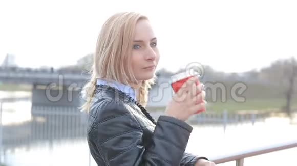 美丽的女孩在街上喝着咖啡看着摄像机视频的预览图
