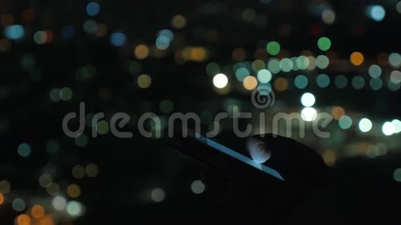 带着手机的女人面对夜晚模糊的城市视频的预览图