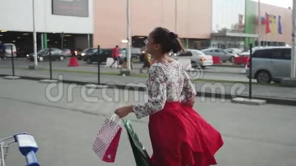 年轻的黑发女人穿着漂亮的连衣裙带着购物袋慢悠悠地走在街上1920x1080视频的预览图