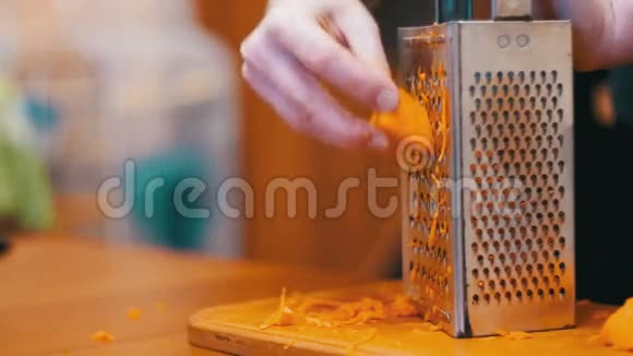 女人的手在家厨房的Grater上摩擦胡萝卜慢动作视频的预览图