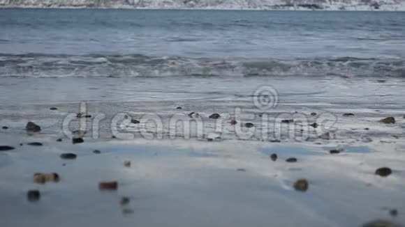 清冽的寒潮在深秋的浅棕色沙质海岸袭来雪山底部背景模糊视频的预览图