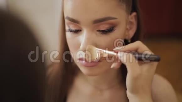 女化妆师使用粉刷美丽的模特在美容工作室专业化妆师完成时装视频的预览图