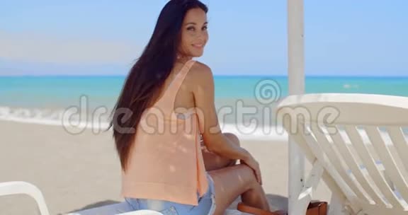 体贴的女人坐在沙滩上的阳光休息室视频的预览图