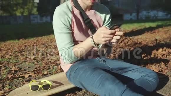 年轻迷人的少年在秋天公园里带着一部智能手机视频的预览图