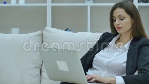 年轻的女商人坐在沙发上手提电脑视频的预览图
