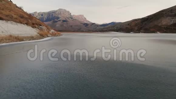 在蓝色日落后在被高加索山脉包围的冰湖上的低空飞行视频的预览图