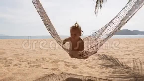 金发小女孩在吊床上翻过棕榈树视频的预览图