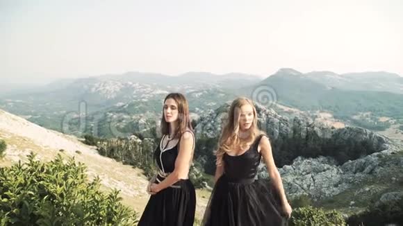 两个穿着时髦黑色礼服的年轻美女在一片山景背景下一起在镜头前摆姿势视频的预览图