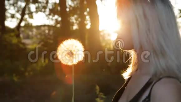 日落时分美丽的女孩在草地上吹蒲公英视频的预览图