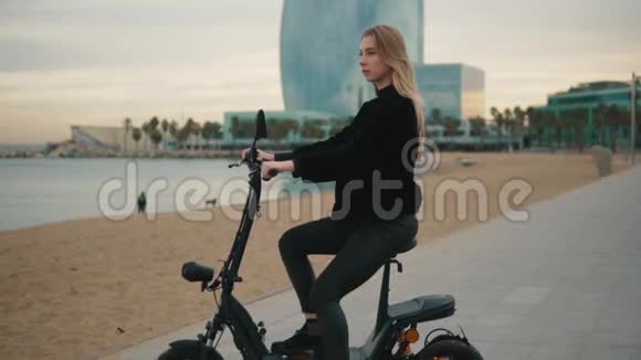 漂亮的金发女人在海边驾驶电动自行车视频的预览图