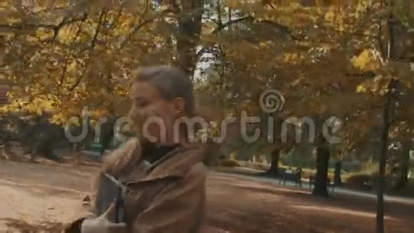 快乐的女人在秋天阳光明媚的公园里快乐地散步视频的预览图