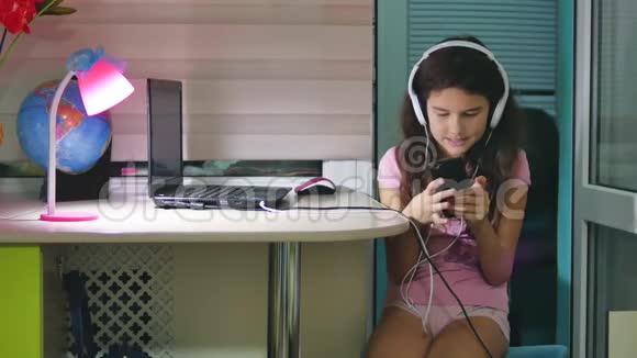 带着耳机坐着玩智能手机的少女在室内玩智能手机的女生视频的预览图