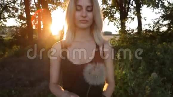日落时分美丽的女孩在草地上吹蒲公英视频的预览图