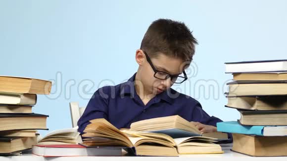 男孩坐在桌子旁疲倦地翻阅一本书蓝色背景视频的预览图