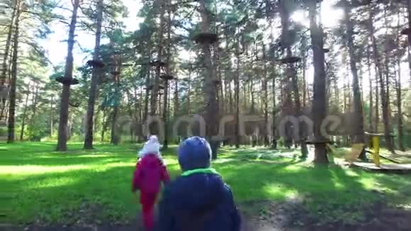 男孩金发女孩戴着眼镜走在绿草上幼儿学习一个大的爬架秋天阳光明媚视频的预览图