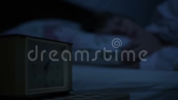 一个穿睡衣的女孩躺在床上看着闹钟睡不着从小时到小时的可变焦点视频的预览图