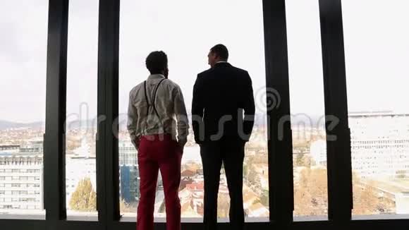 两个商人透过窗户望着城市说话视频的预览图
