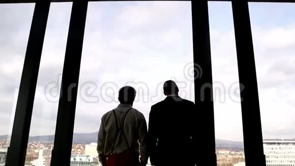 两个商人透过窗户看着城市视频的预览图