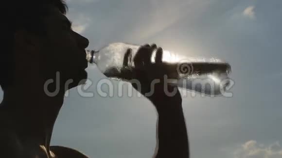 年轻人从自然界的塑料瓶里喝水日落时分有水的家伙背景中的太阳视频的预览图