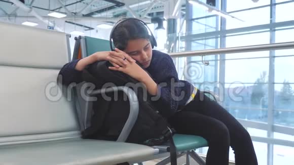 戴着耳机的少女睡在机场等待飞机起飞登机门长椅上的生活方式视频的预览图