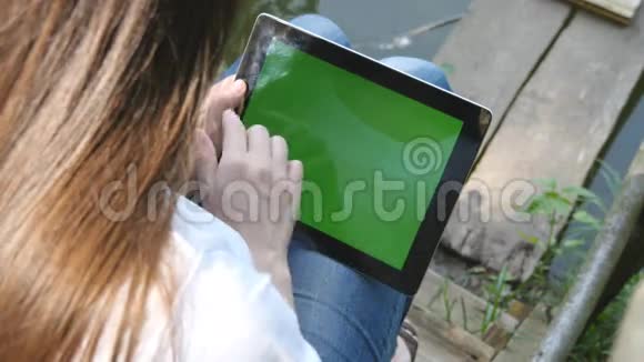 女性手使用数字平板电脑绿色屏幕坐在湖边的木制码头视频的预览图