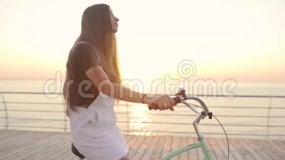 年轻的美女骑着自行车在日落或日出的时候在海边玩得很开心视频的预览图