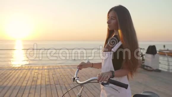 年轻的美女骑着自行车在日落或日出的时候在海边玩得很开心视频的预览图