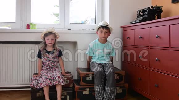 可爱的小女孩和男孩坐在老式手提箱上等待开始度假小女孩穿花裙子视频的预览图