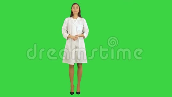 微笑着穿着实验室外套的漂亮女人在绿色屏幕上与摄像机交谈Chroma键视频的预览图