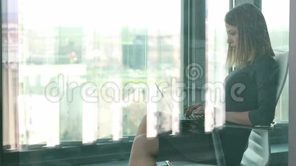 女商人坐在玻璃墙后面的椅子上一边打手提电脑视频的预览图