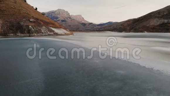 在蓝色日落后在被高加索山脉包围的冰湖上的低空飞行视频的预览图